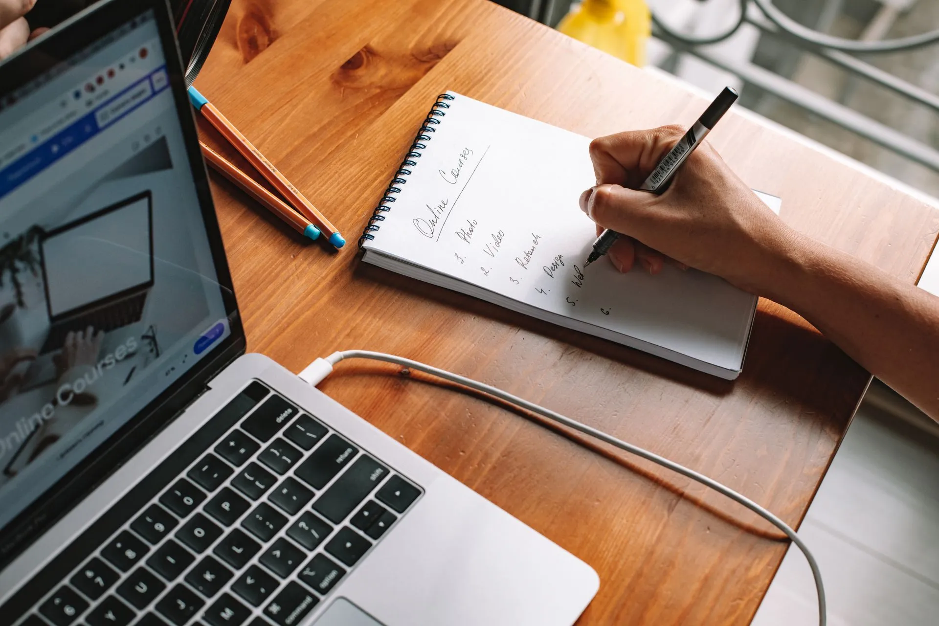 Persona anotando ideas en un cuaderno junto a su laptop