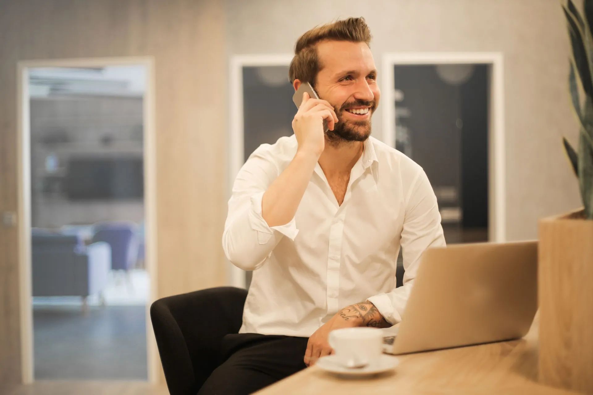 Hombre sonriendo mientras habla por celular frente a su laptop