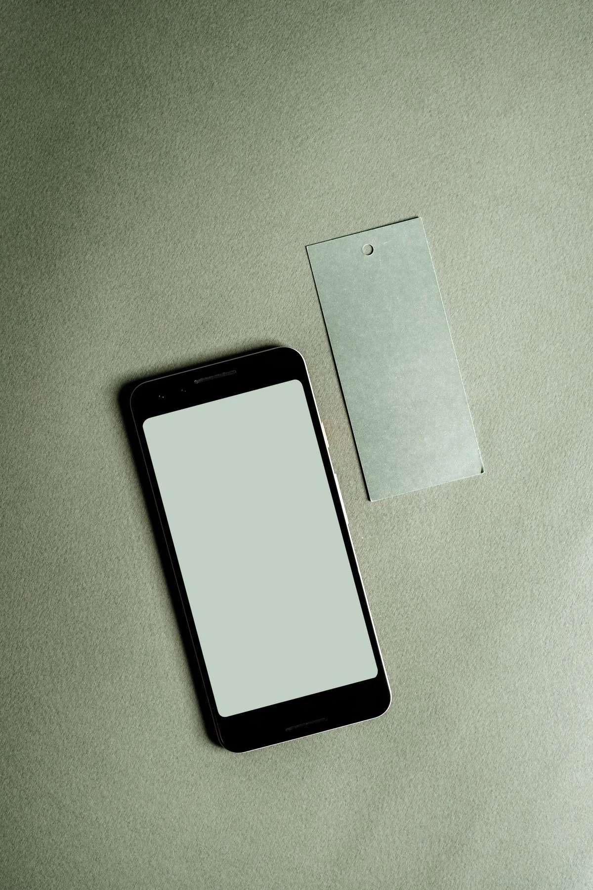 Celular junto a una etiqueta en blanco sobre una superficie verde